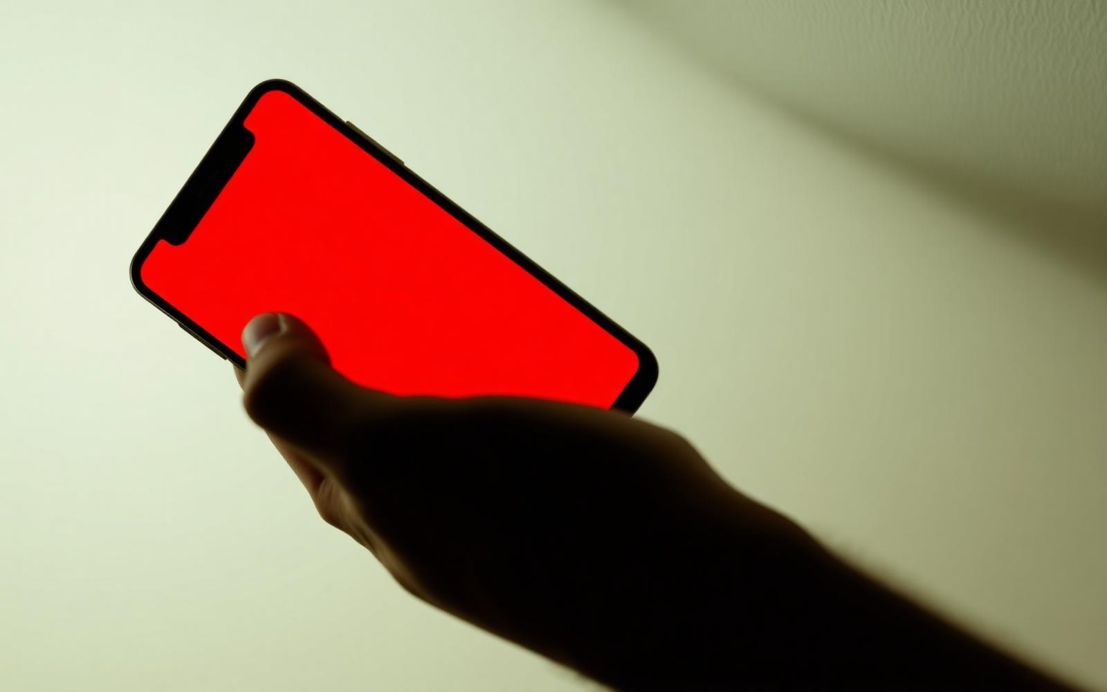 A hand holding a phone with a glowing red screen